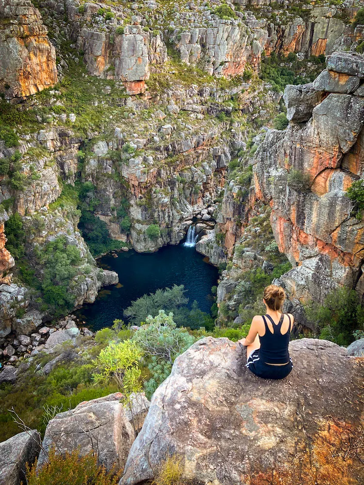A hiker sitting on a rock overlooking a deep clear pool and waterfall in the Groot Winterhoek mountains