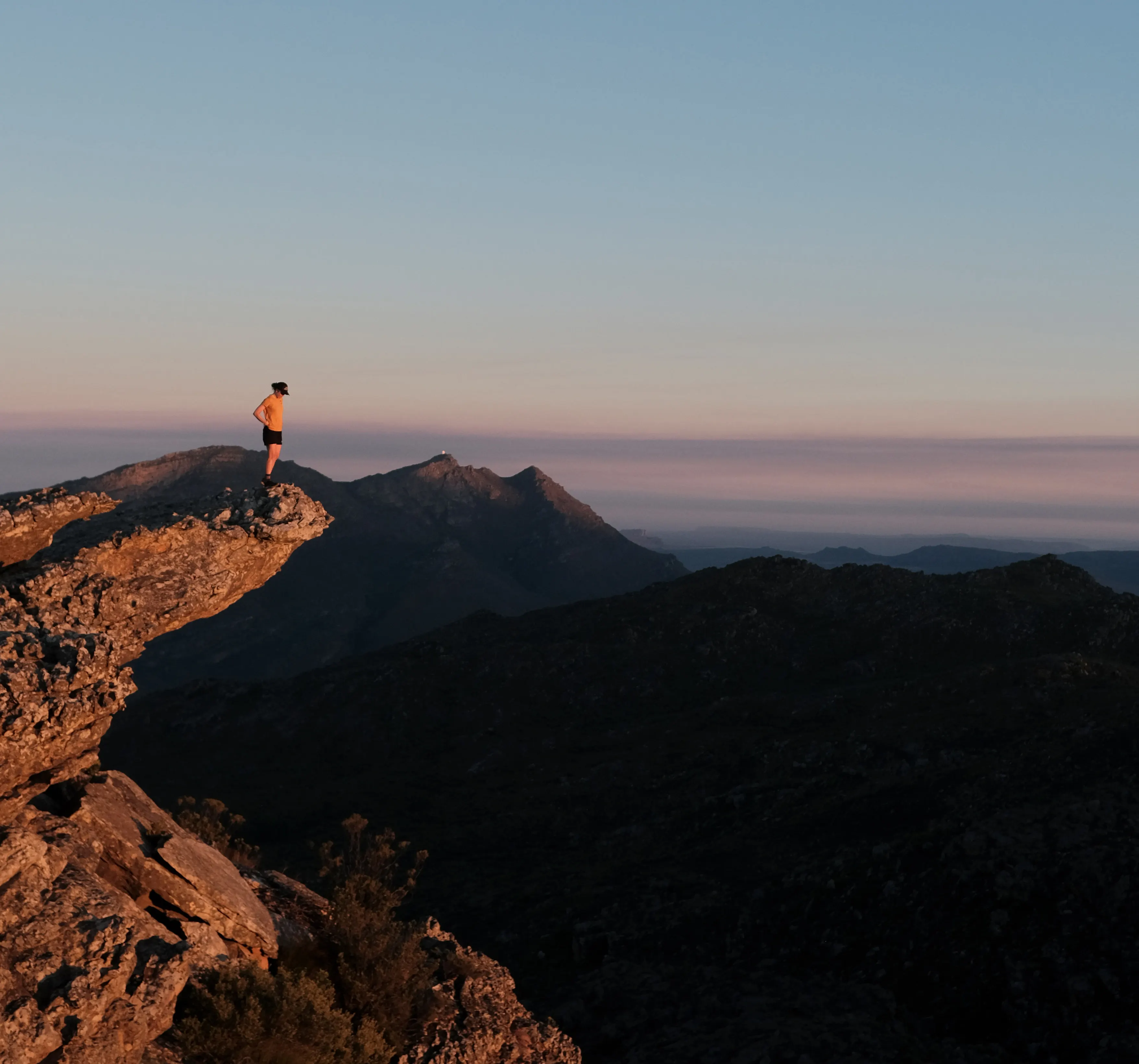 A hiker standing on a rocky ridge above the clouds at sunset in the Western Cape mountains